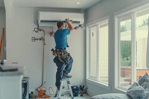 Un technicien installant une climatisation réversible sur un mur blanc.
